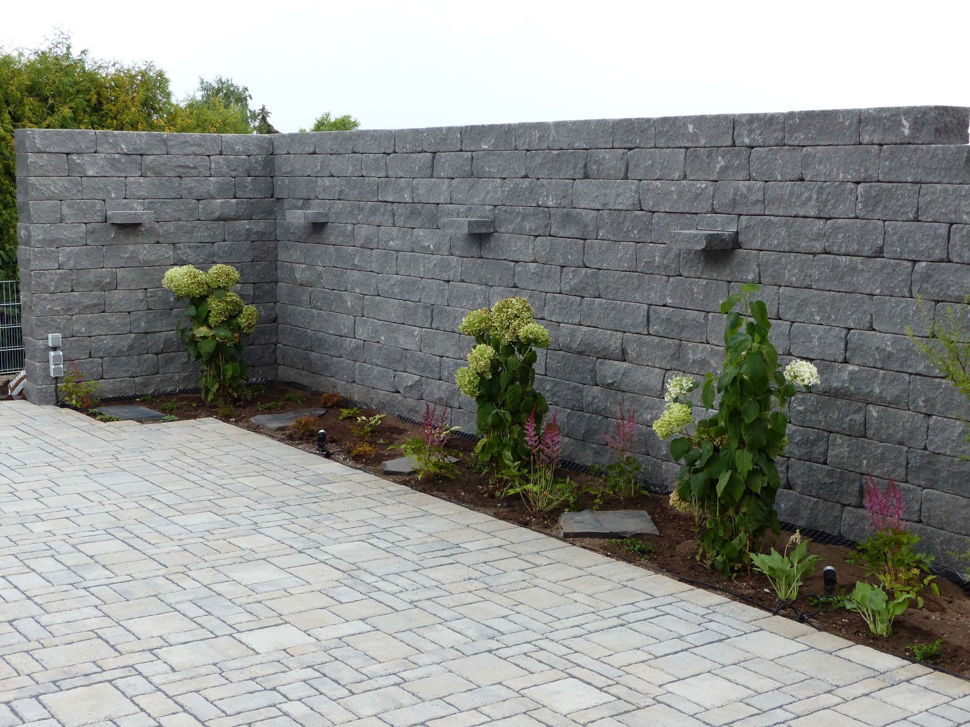 Mauer aus Pflastersteinen vor kleinem Blumenbeet