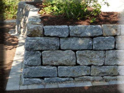 Natursteinmauer auf gepflastertem Hof mit Grünstreifen